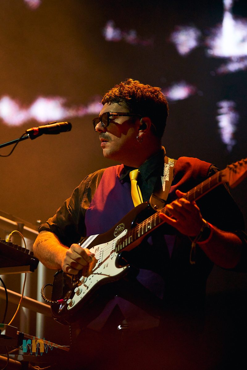 El guitarrista de Cervatana toca con gafas oscuras y corbata amarilla bajo luz ámbar en Canela Party 2026.