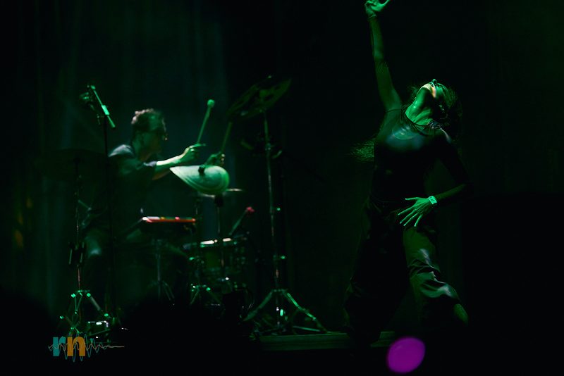 La vocalista de Cervatana alza un brazo mientras el percusionista toca bajo luz verde en Canela Party 2026.