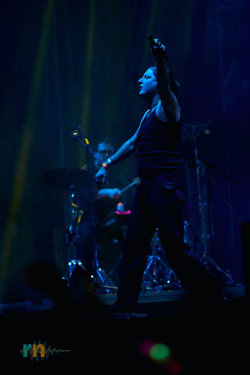 La vocalista de Cervatana alza el micrófono bajo haces de luz azul en Canela Party 2026.