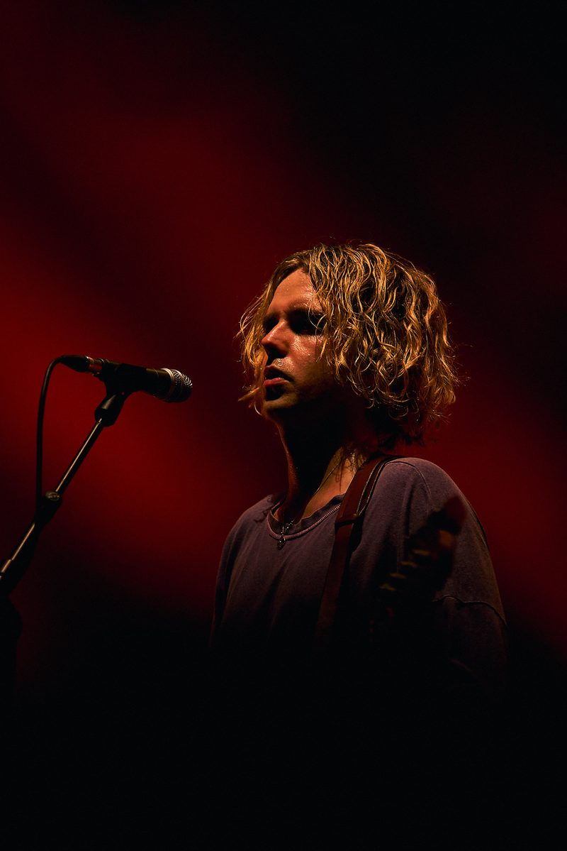 A Fontaines D.C. guitarist sings at the microphone under intense red light in Alicante, Spain.