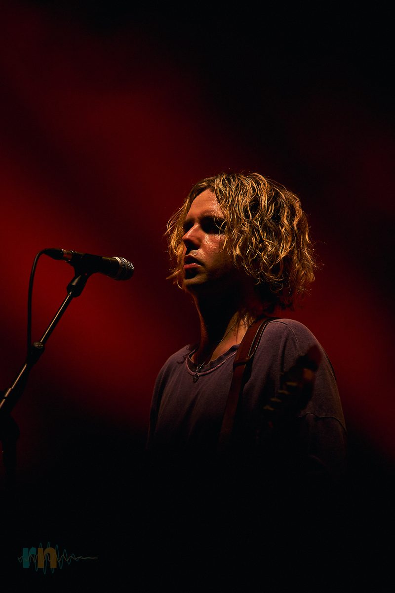 A Fontaines D.C. guitarist sings at the microphone under intense red light in Alicante, Spain.