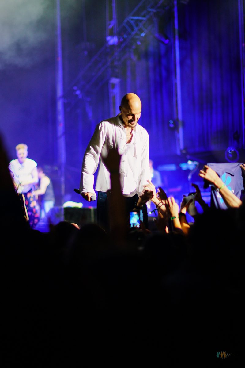 Tim Booth canta junto al público con las manos alzadas