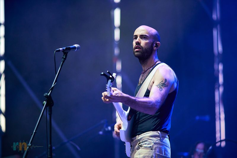 Cantante y guitarrista de La Milagrosa toca una guitarra blanca ante el micrófono bajo luz azul en Alicante.