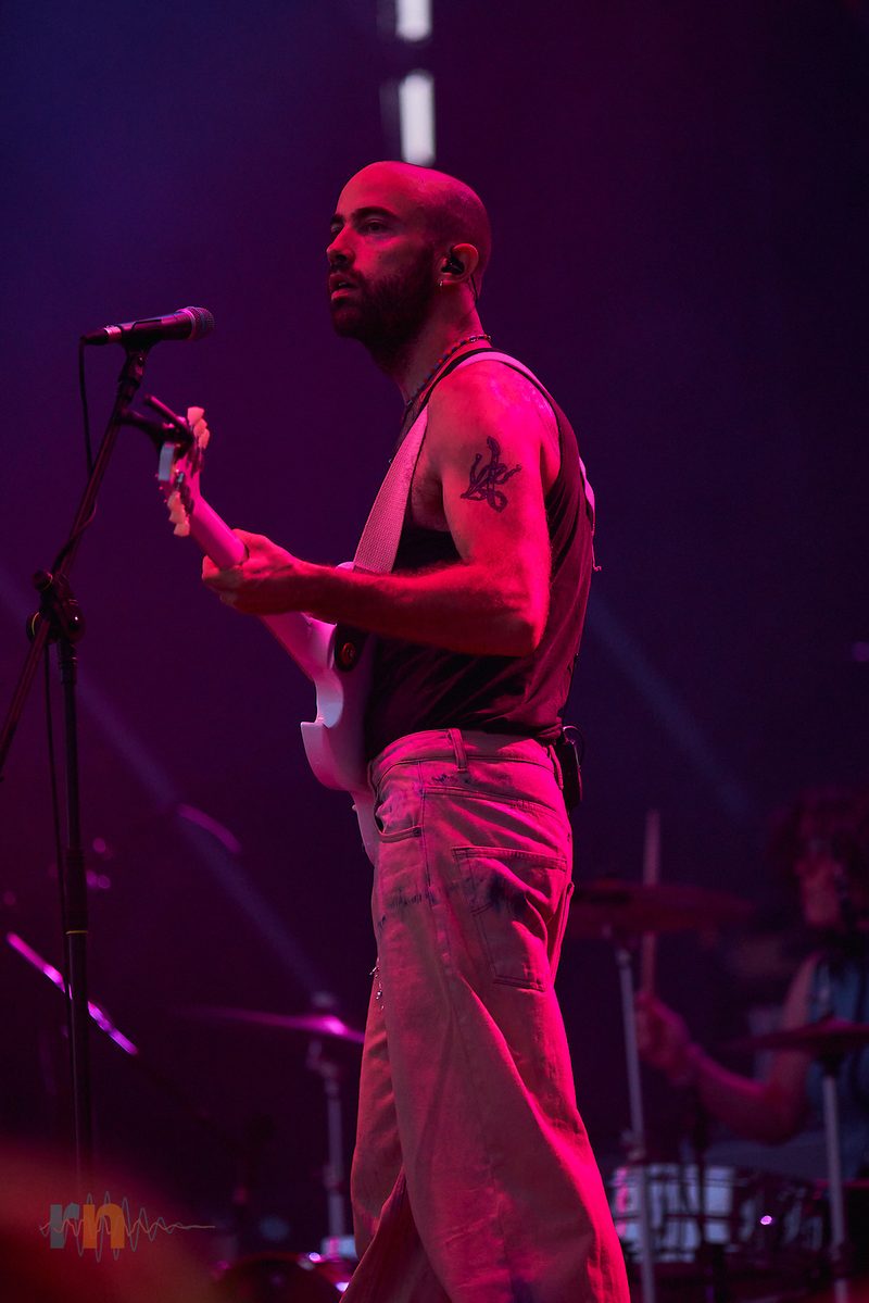 Cantante de La Milagrosa toca la guitarra de perfil bajo una intensa iluminación magenta.