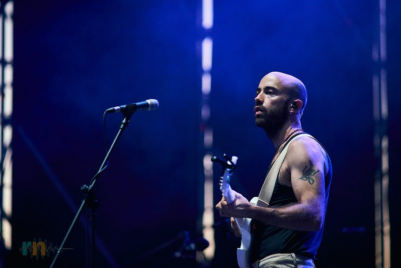 Cantante y guitarrista de La Milagrosa espera junto al micrófono rodeado de luz azul.