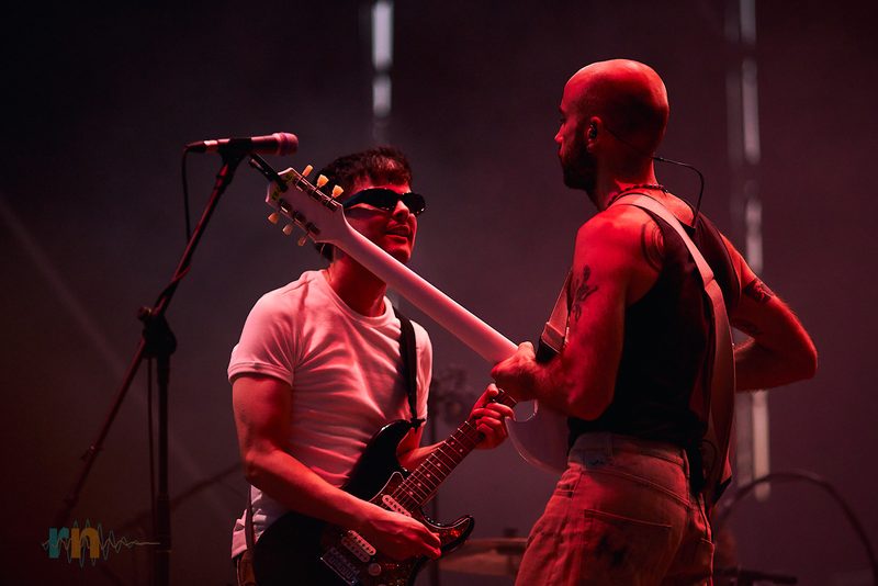 Dos guitarristas de La Milagrosa se encaran mientras tocan bajo una intensa luz roja.