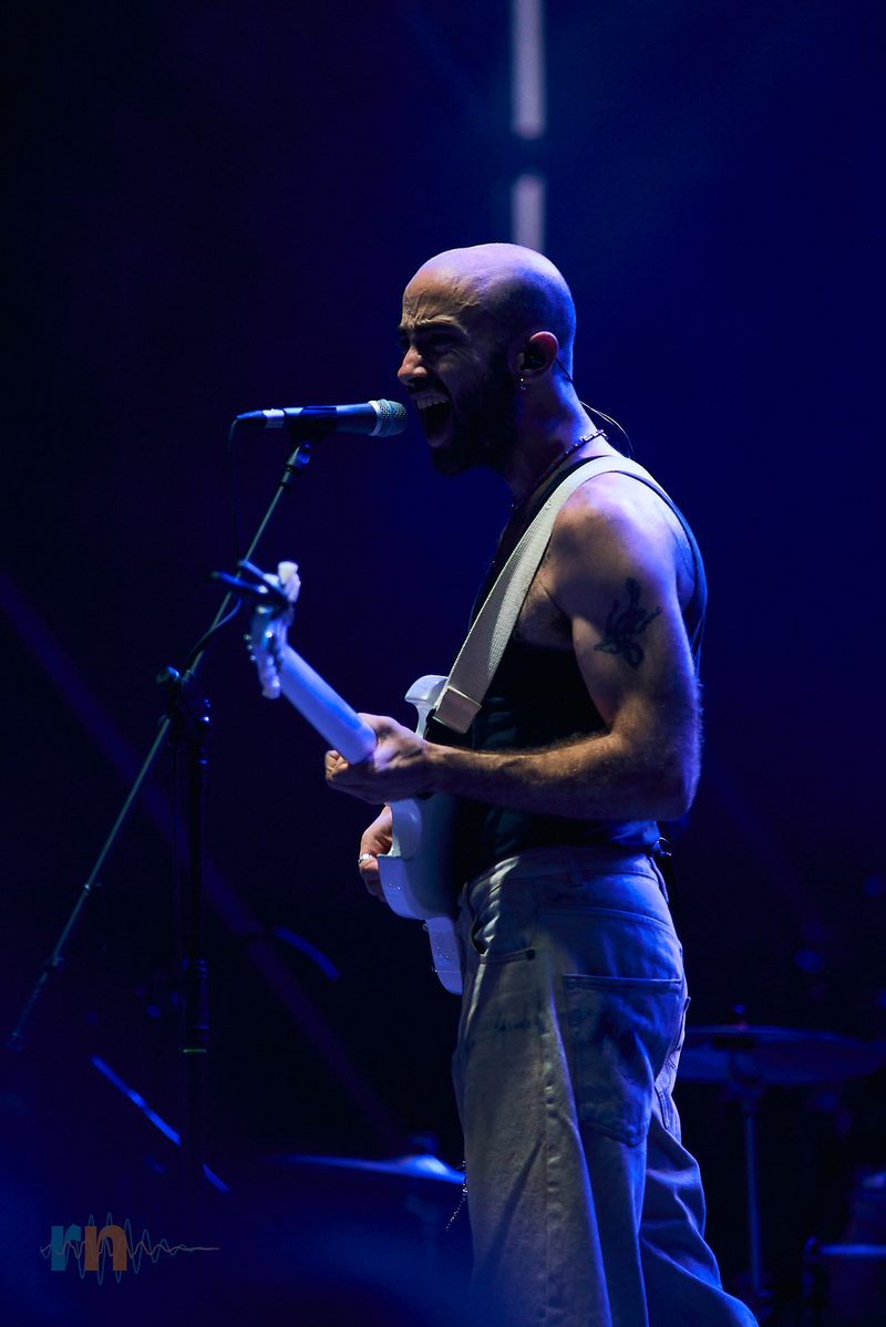 Cantante de La Milagrosa canta y toca la guitarra bajo un foco azul en El Muelle Live.