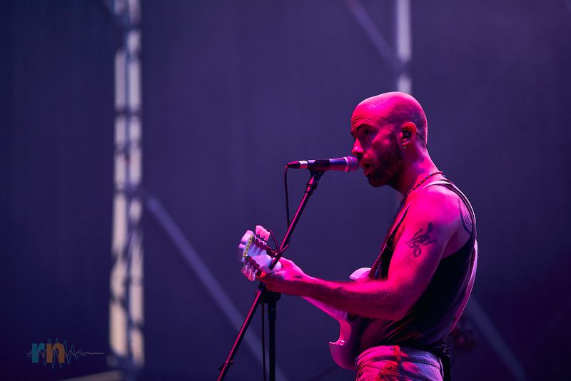 Cantante de La Milagrosa interpreta una canción con la guitarra envuelto en luz magenta.