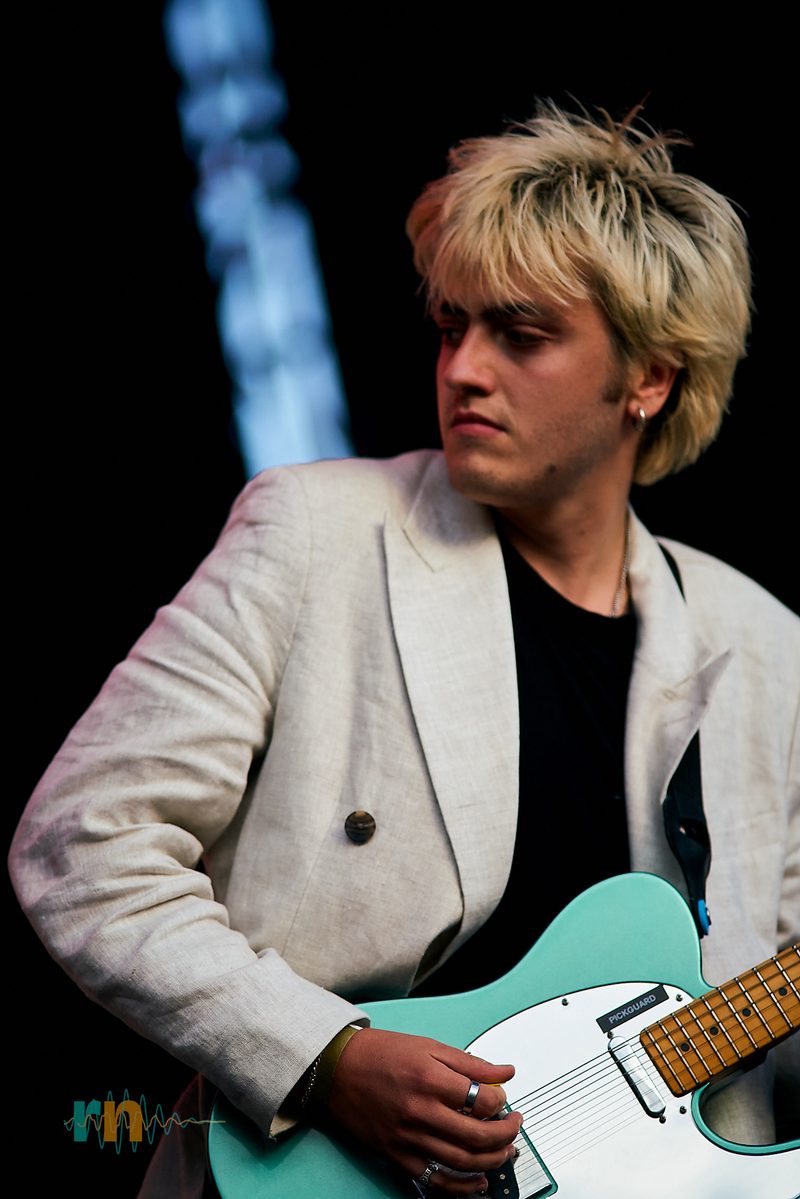 Un guitarrista de Man/Woman/Chainsaw toca una guitarra turquesa con chaqueta blanca en Canela Party 2026.