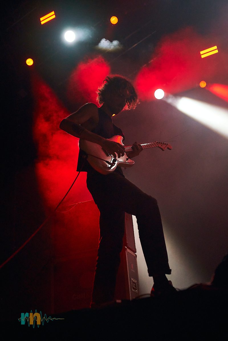 The MAQUINA. guitarist plays amid red haze and white beams at Canela Party 2026.
